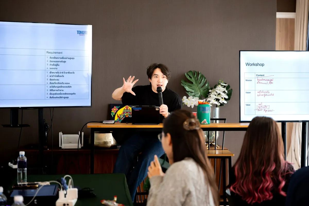 ผู้สอนถือไมค์สอนหน้าสไลด์ Workshop ขณะที่ผู้เรียนนั่งฟัง